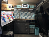 Cozy RV rental interior with a compact kitchen, colorful bed, tiled backsplash, and thoughtful storage solutions.