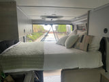 Comfortable RV rental interior: A cozy bed with white and green bedding, overhead storage, and front view.