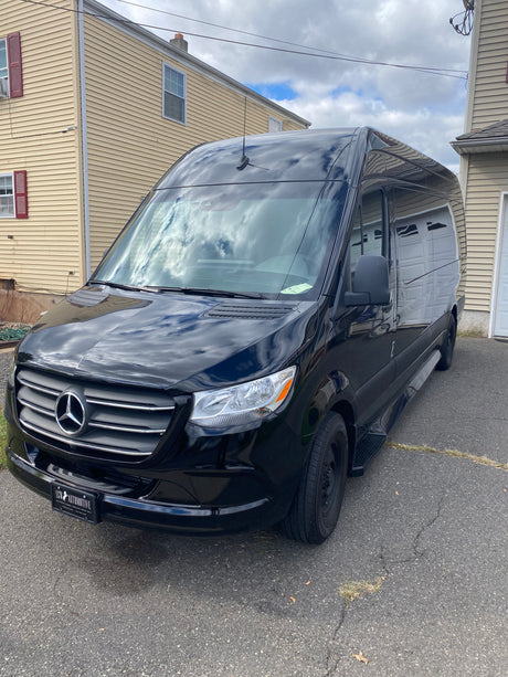 Black Mercedes-Benz Sprinter van, often used for luxury travel or RV rental, parked on a driveway.