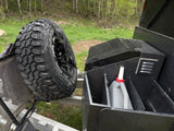RV rental's rugged spare tire & storage box with jerrycan, set against a wooded backdrop.