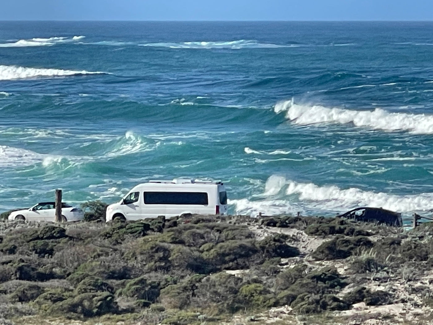 Scenic coastal view: an RV rental and other vehicles parked on a bluff overlooking the ocean with breaking waves. — photo 2