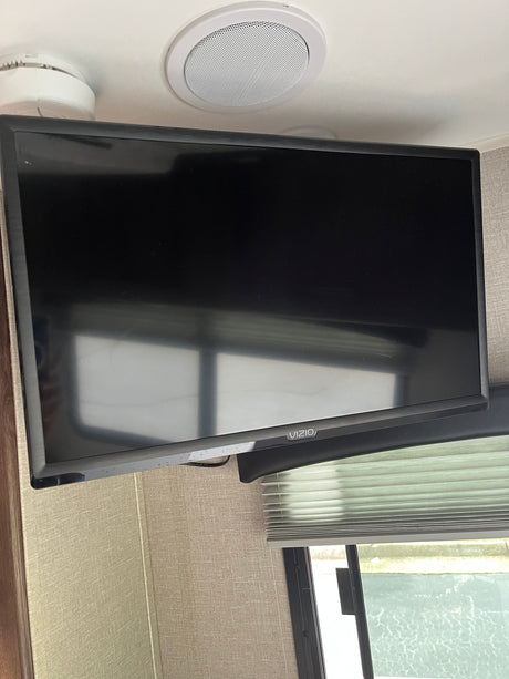 RV rental interior featuring a Vizio TV mounted high, with a ceiling speaker and smoke detector above, and blinds below.