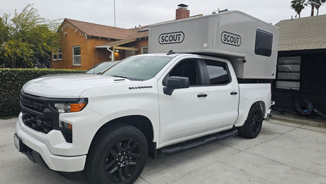 White Chevrolet Silverado pickup truck with a "Scout" brand truck camper, ideal for RV rental.