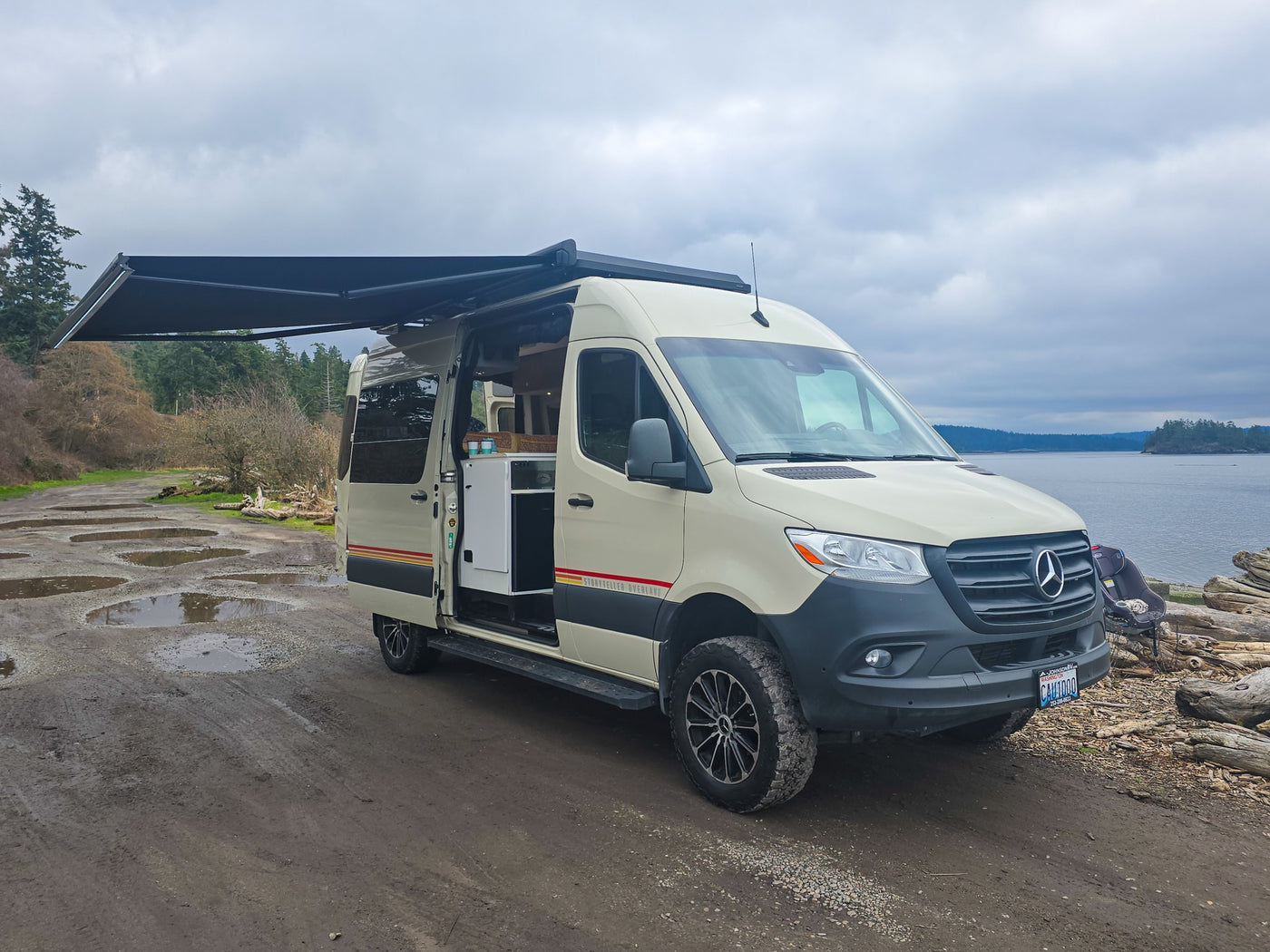 Spacious RV rental van with awning extended, parked on a muddy road by the water. Interior visible for comfortable van life. — photo 4