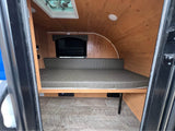 Compact RV rental interior featuring a wood-paneled, curved ceiling, a comfortable bed, and a skylight.