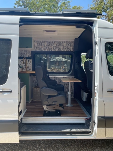 Bright RV rental interior with wood flooring, a swiveling seat, and a compact dining/workspace in a modern camper van. — photo 7