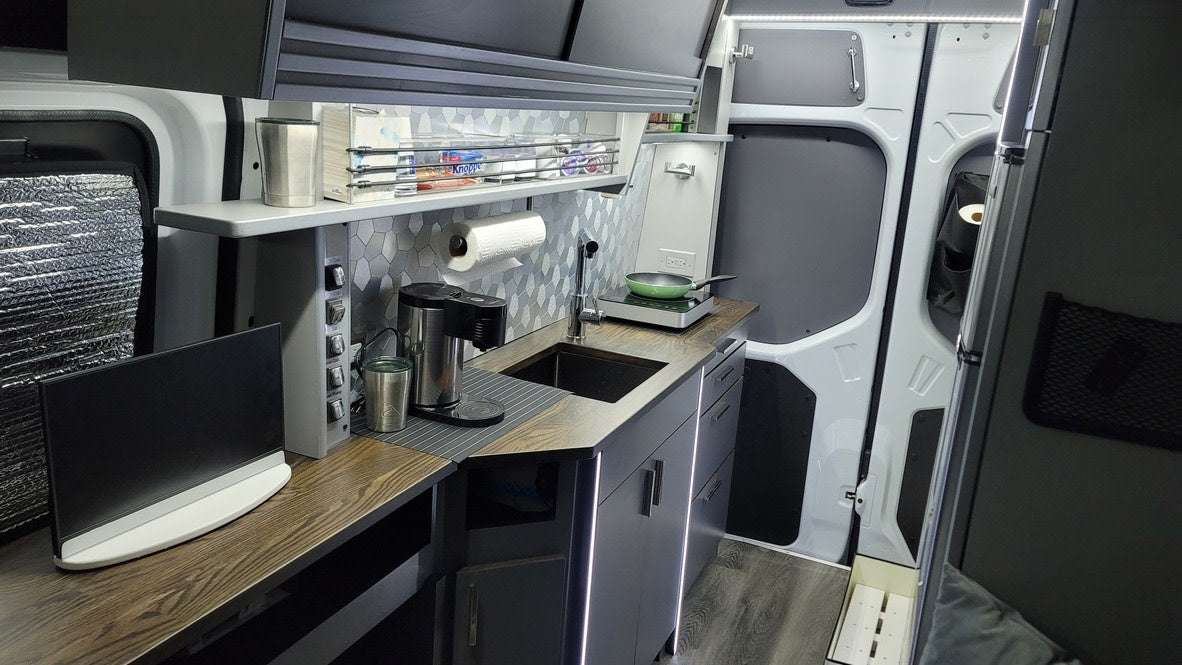 This modern RV rental interior features a sleek camper kitchen with sink, induction cooktop, coffee maker, and LED lighting.