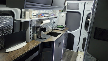 This modern RV rental interior features a sleek camper kitchen with sink, induction cooktop, coffee maker, and LED lighting.