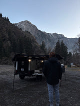 Adventure camping setup! Man stands by his compact RV rental trailer in a scenic mountain landscape.