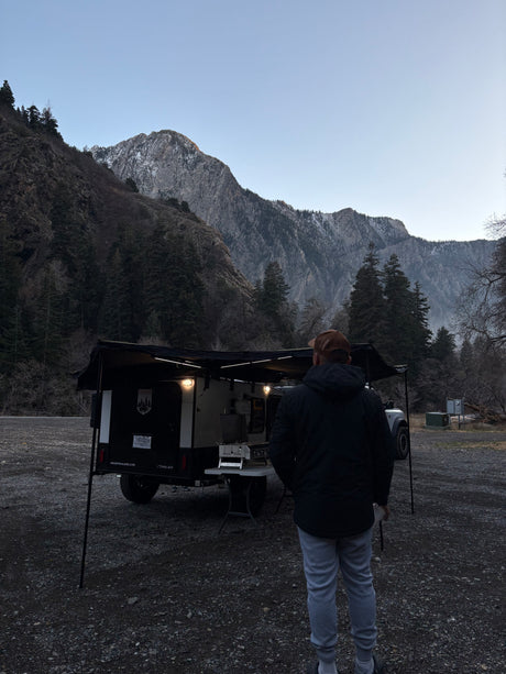 Adventure camping setup! Man stands by his compact RV rental trailer in a scenic mountain landscape.