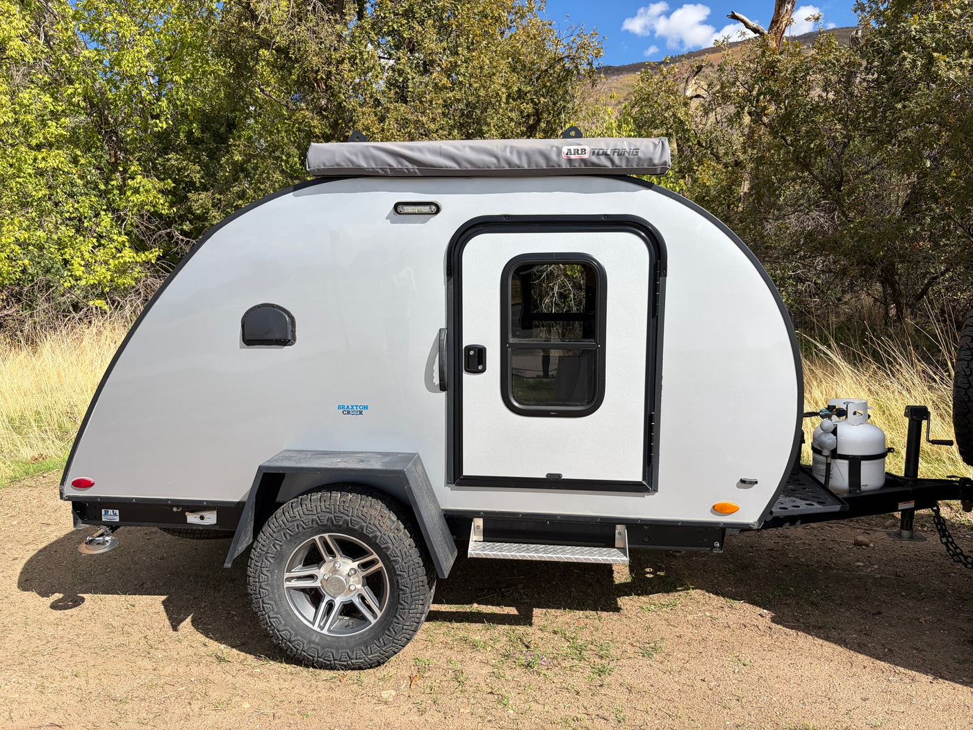  ideal for outdoor adventures.|Gray Braxton Creek teardrop camper shown in nature. This compact RV rental features off-road tires and an ARB awning — photo 2