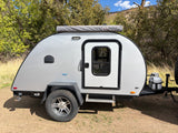 Gray Braxton Creek teardrop camper shown in nature. This compact RV rental features off-road tires and an ARB awning, perfect for camping.