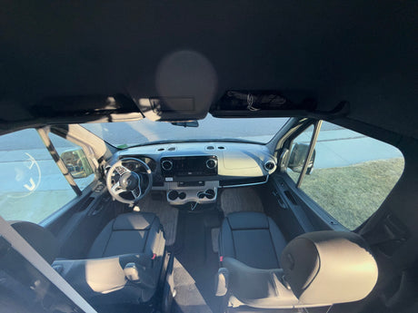 Interior of an RV rental: Wide view of the spacious front cabin with dashboard, steering wheel, and two front seats.