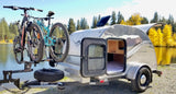 Teardrop camper **rv rental** with bikes by a scenic lake. Features solar panel & comfy bed for outdoor adventures.
