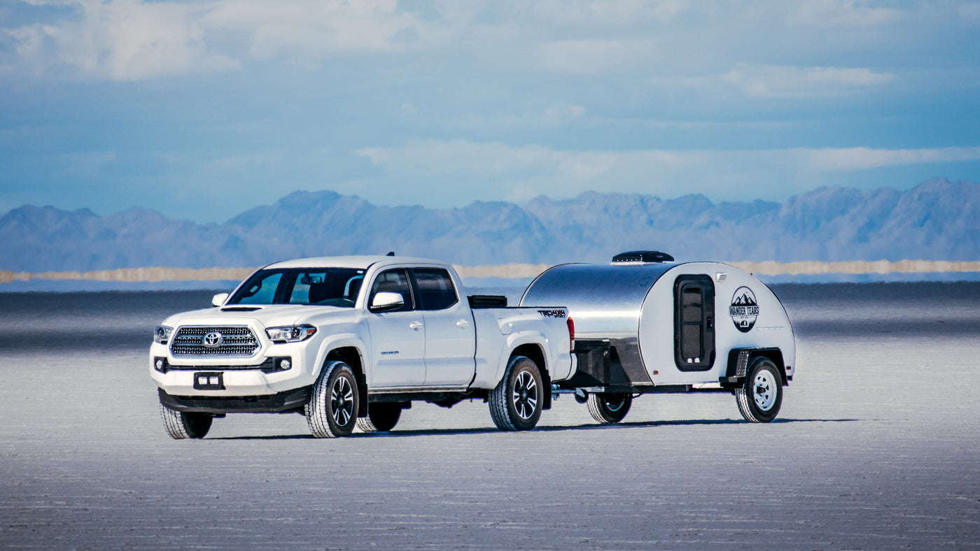 White pickup truck and shiny teardrop RV rental on salt flats with mountains under a blue sky. — photo 3
