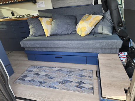 Cozy RV rental interior with blue sofa, kitchen, and smart drawer storage. Ideal for adventures.