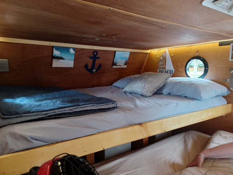 Cozy RV rental bunk beds feature nautical decor, warm lights, and a porthole window. Perfect for your travel comfort. — photo 9
