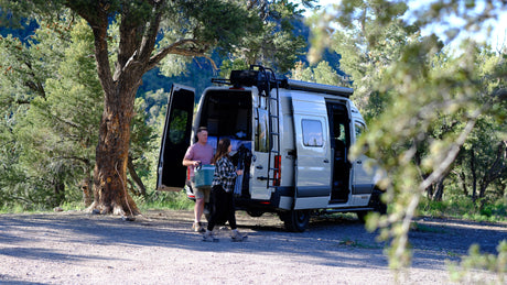 A couple unpacks their rv rental in a scenic forested area, preparing for an outdoor adventure.