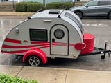 Stylish silver & red teardrop RV rental, parked on a wet street. Ready for your next adventure.