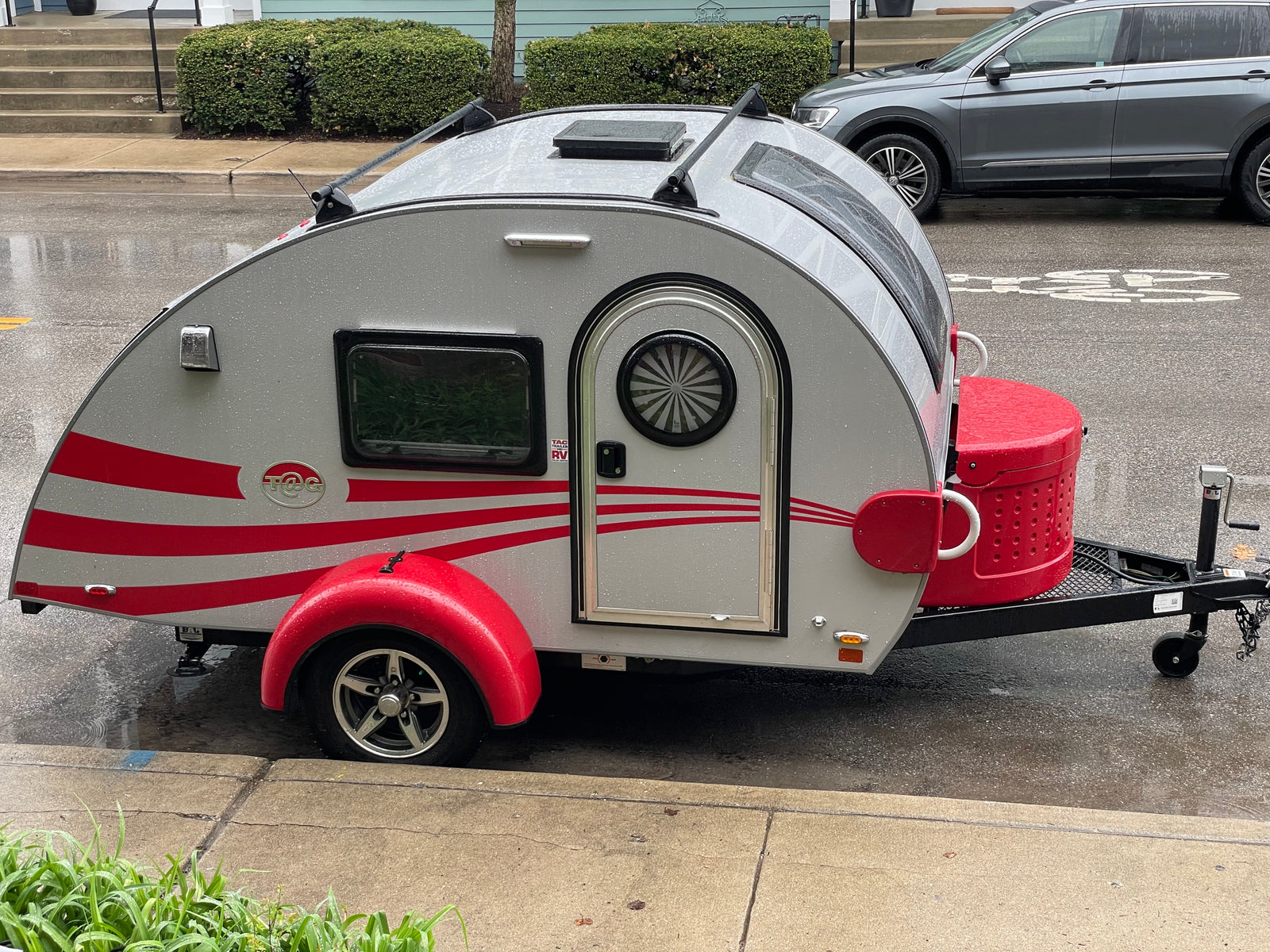 Stylish silver & red teardrop RV rental, parked on a wet street. Ready for your next adventure.