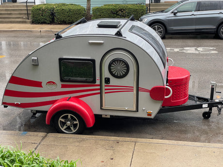 Stylish silver & red teardrop RV rental, parked on a wet street. Ready for your next adventure.