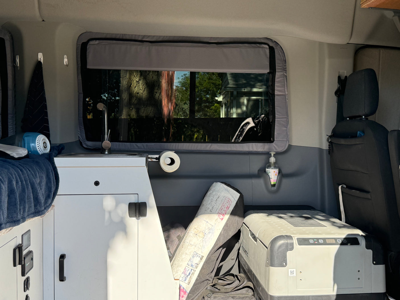 Tour an RV rental's cozy interior: sink, hand soap, Dometic cooler, Coleman table, and window views.