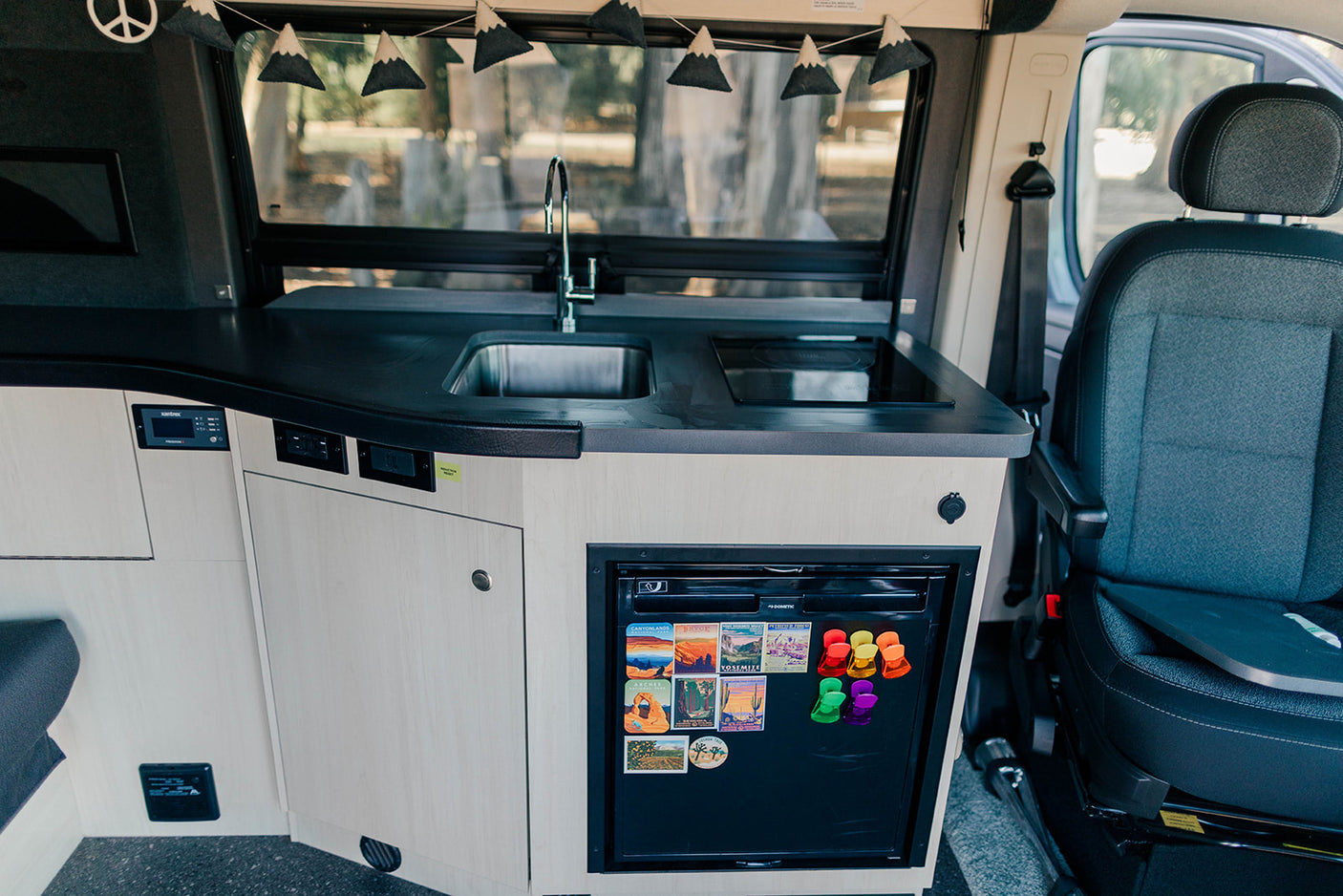 Experience RV rental comfort: a sleek camper van kitchen featuring a sink, induction cooktop, and fridge with magnets.