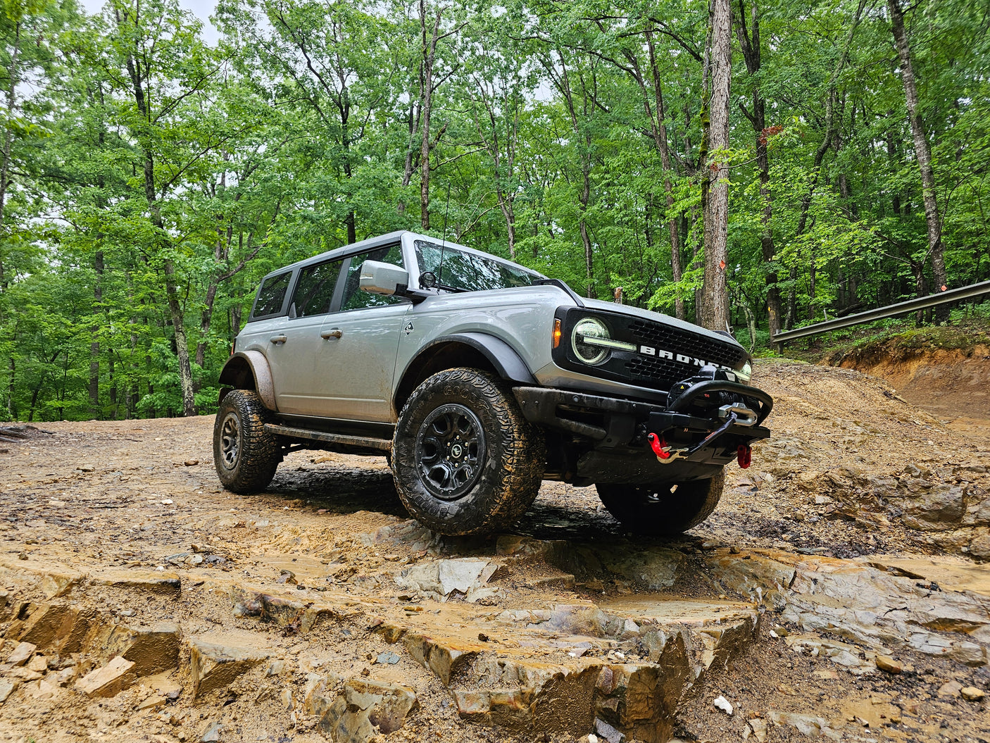 Grey Ford Bronco conquers a rocky, muddy forest trail. A rugged adventure, quite different from an RV rental vacation.