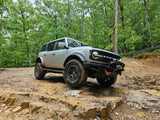 Grey Ford Bronco conquers a rocky, muddy forest trail. A rugged adventure, quite different from an RV rental vacation.