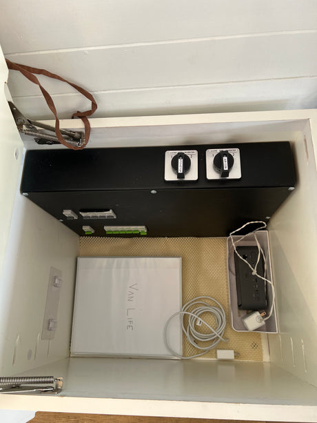 RV rental power control unit with shore/inverter switches for stovetop & AC, plus cables & 'VAN LIFE' guide in storage.