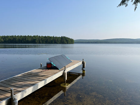 Enjoy off-grid RV rental adventures. Portable solar panel and power station on a tranquil lake dock, surrounded by forests.