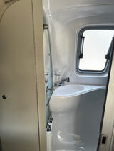Inside an RV rental, a bright, compact washroom with a white sink, mirror, and window providing natural light.
