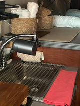 Inside an RV rental: a compact kitchen sink with a modern faucet, roll-up drying rack, and storage baskets for linens.