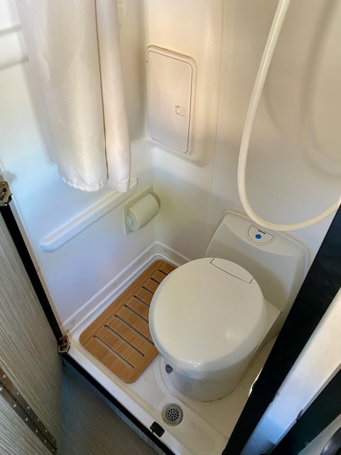 Compact RV rental wet bath featuring a toilet, shower, bamboo mat, and toilet paper holder. Ideal for road trips. — photo 14