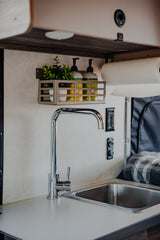 This RV rental offers a well-equipped compact kitchen: stainless steel sink, modern faucet, and organized wall storage for essentials.