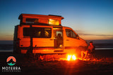 Perfect RV rental adventure: a campervan on a sandy beach at dusk, with a cozy campfire and a person relaxing by the ocean.