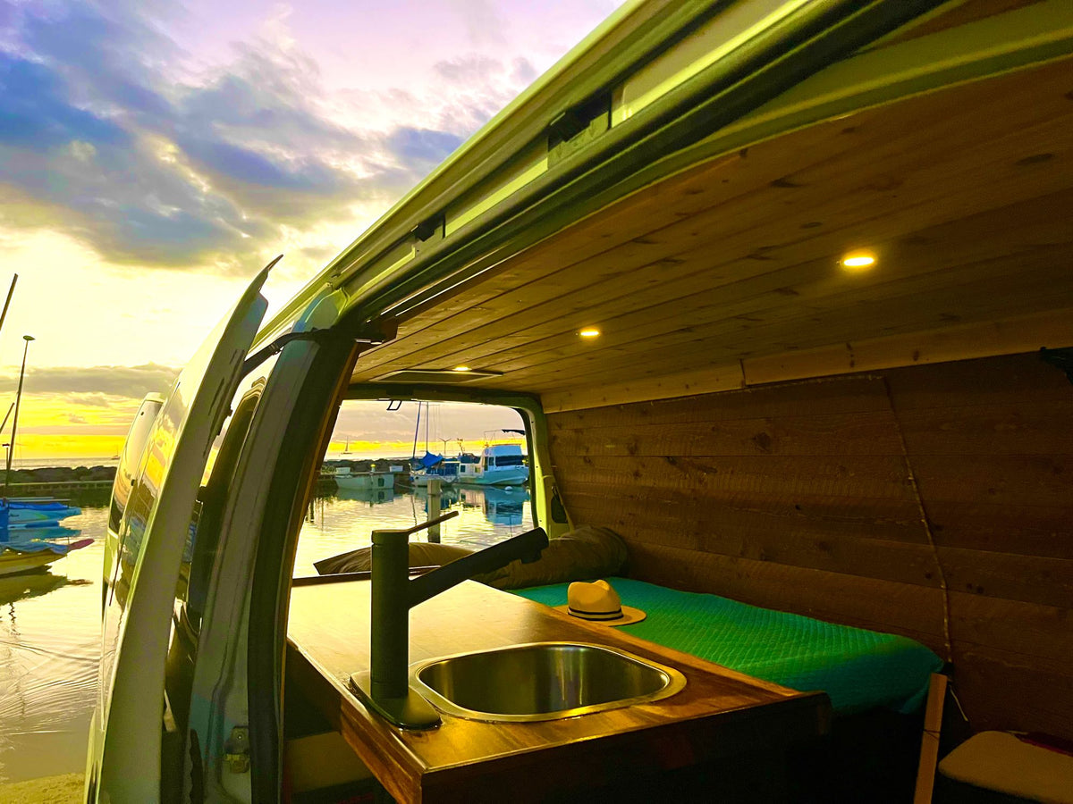  a cozy wood-paneled van interior overlooks a serene waterfront sunset with boats & dock. Perfect for travel.|Cozy camper van interior with kitchen — photo 3