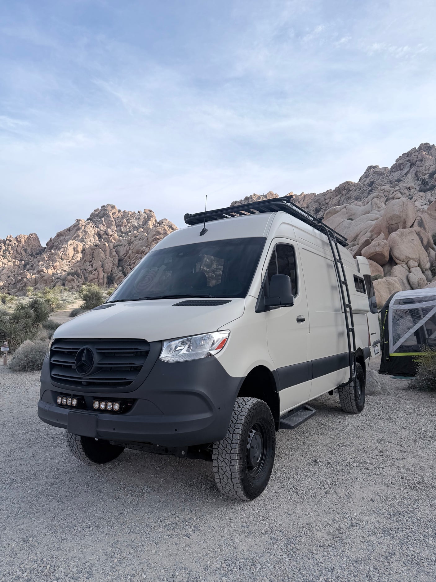 White off-road RV rental van in a rocky desert camp. Ideal for adventure travel and exploring remote landscapes.