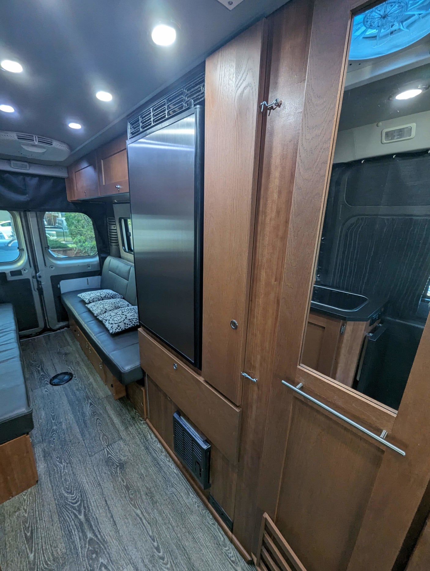 Comfortable RV rental van interior with a kitchen, fridge, wooden cabinets, and versatile seating. Ready for adventure!
