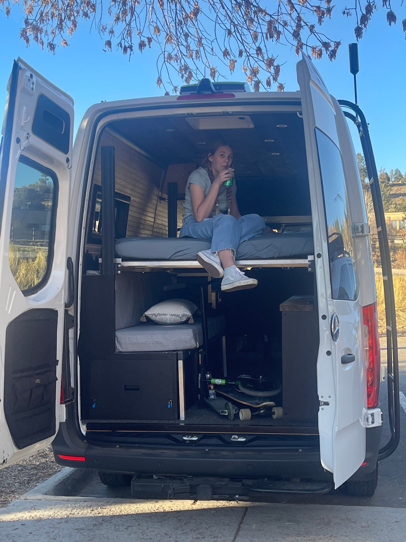 Custom camper van RV rental interior: a woman relaxes on the bed with skateboards stored below. — photo 11