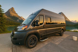 Explore stunning landscapes! Dark grey RV rental parked by a serene mountain lake at golden hour, surrounded by peaks.