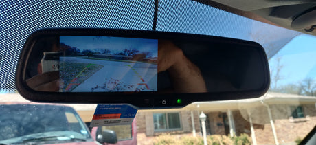 A car's rearview mirror with backup camera display and NTTA sticker. This safety feature is essential for parking, especially with an RV rental.