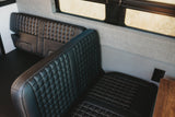 Comfortable black quilted leather seating in this modern RV rental, featuring soft grey fabric walls and a window.