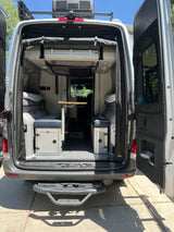 RV rental: Rear view of camper van interior with open doors, showcasing convertible bed, table, and built-in storage.