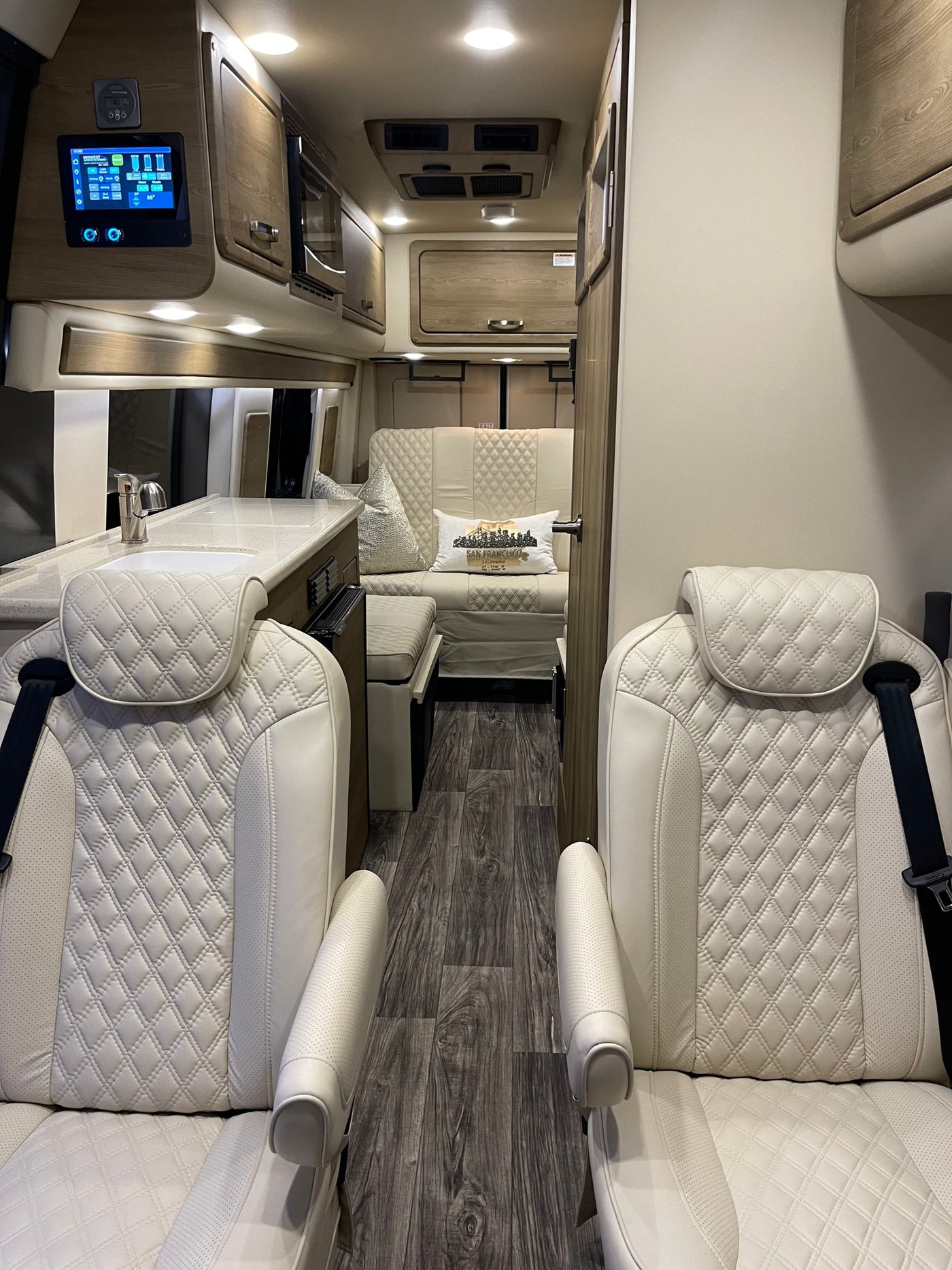 Luxury RV rental interior: white quilted captain's chairs, modern kitchen, and comfortable lounge area. — photo 3