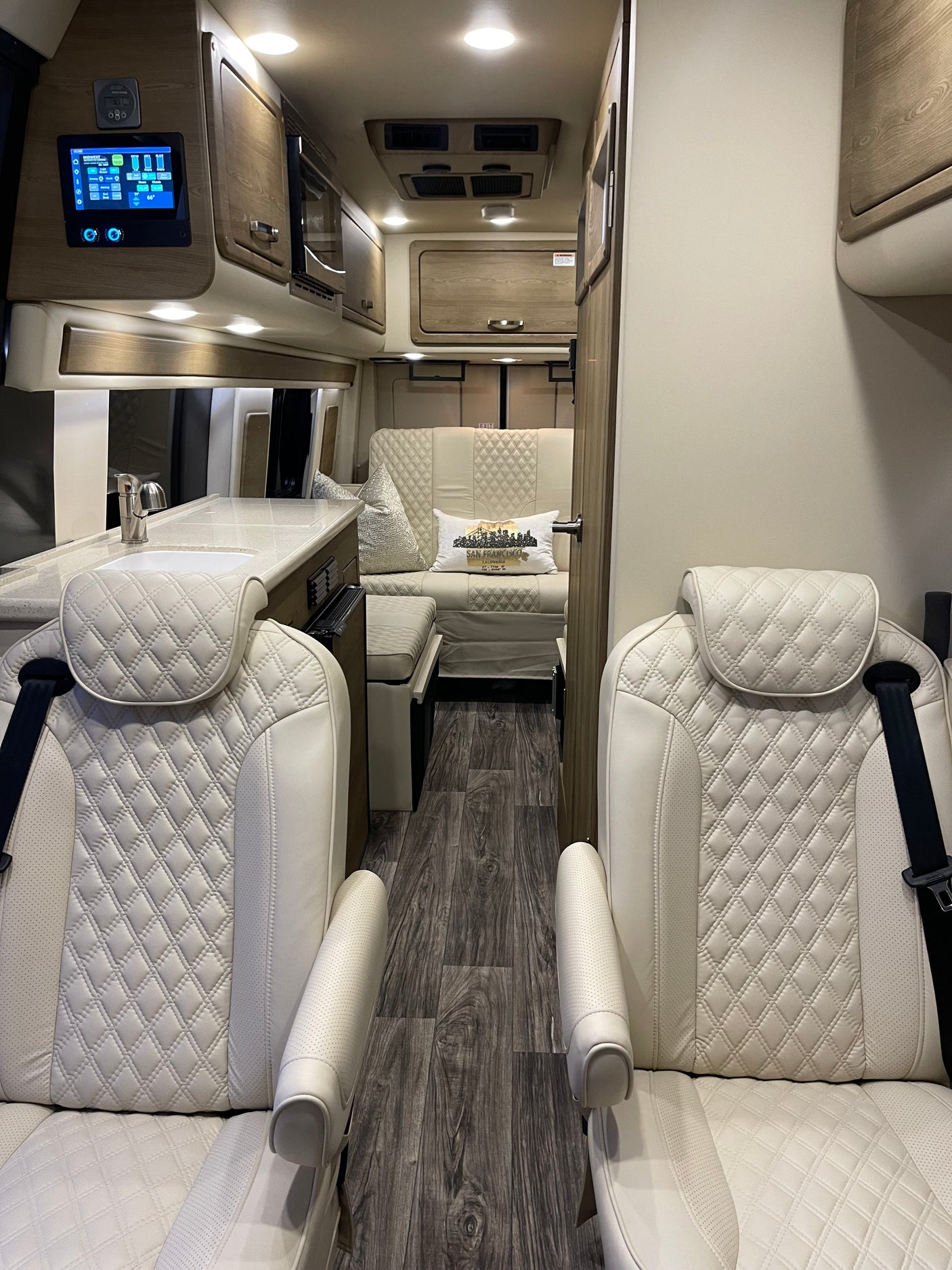 Luxury RV rental interior: white quilted captain's chairs, modern kitchen, and comfortable lounge area.