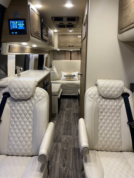 Luxury RV rental interior: white quilted captain's chairs, modern kitchen, and comfortable lounge area.