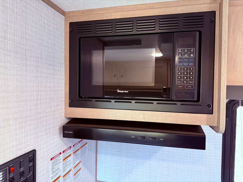 RV rental kitchen interior: a sleek black built-in microwave and range hood framed by light wood cabinetry. — photo 6