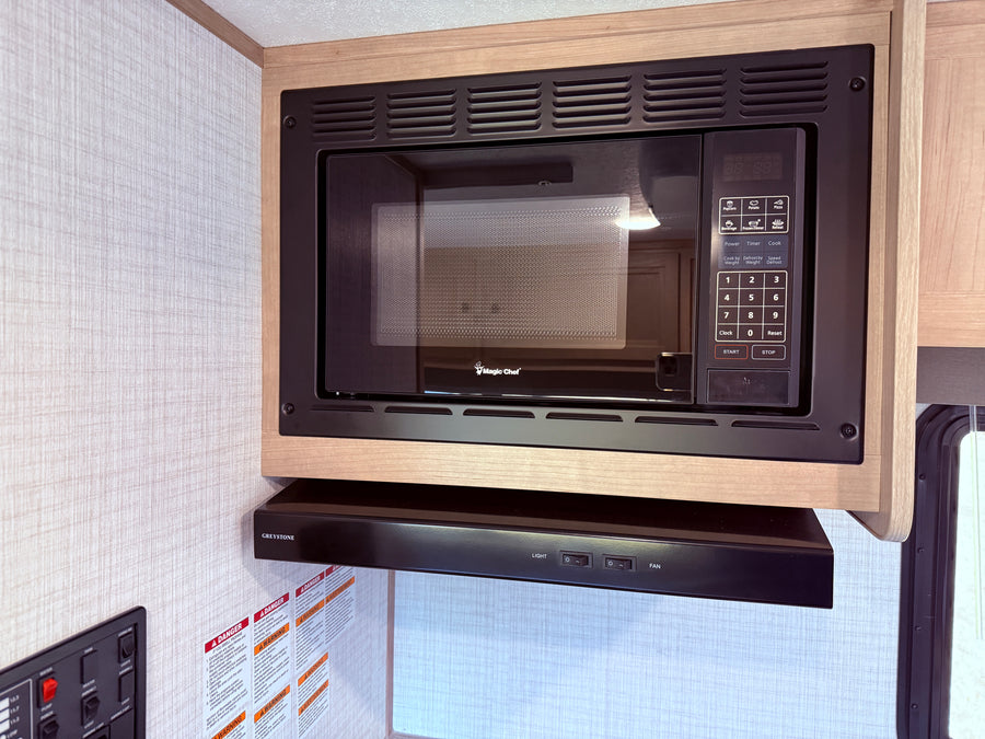 RV rental kitchen interior: a sleek black built-in microwave and range hood framed by light wood cabinetry.