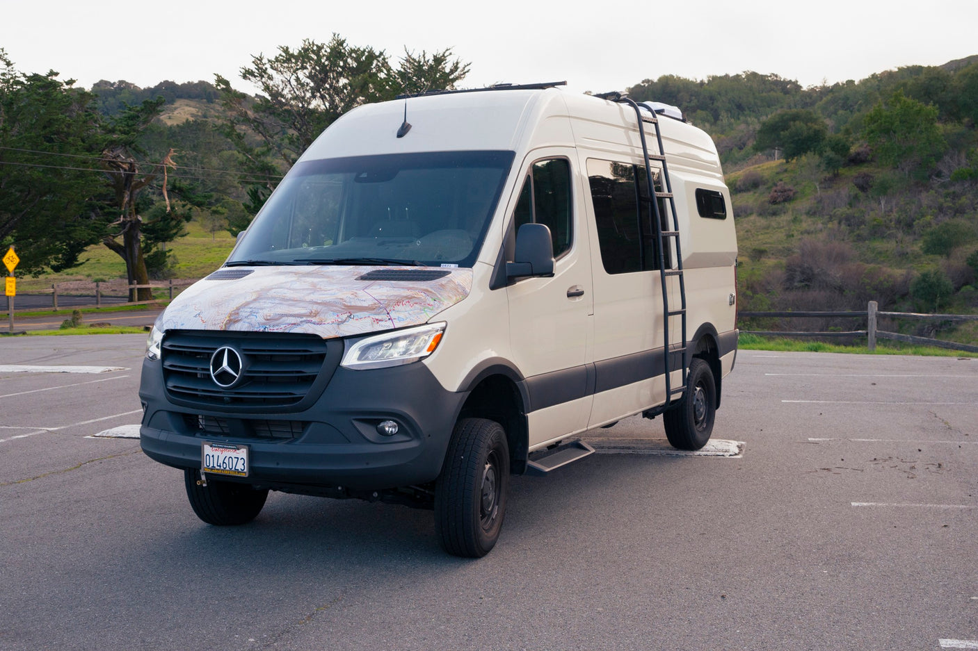 This Mercedes Sprinter camper van rv rental, customized with a map graphic & roof ladder, is parked for adventure.
